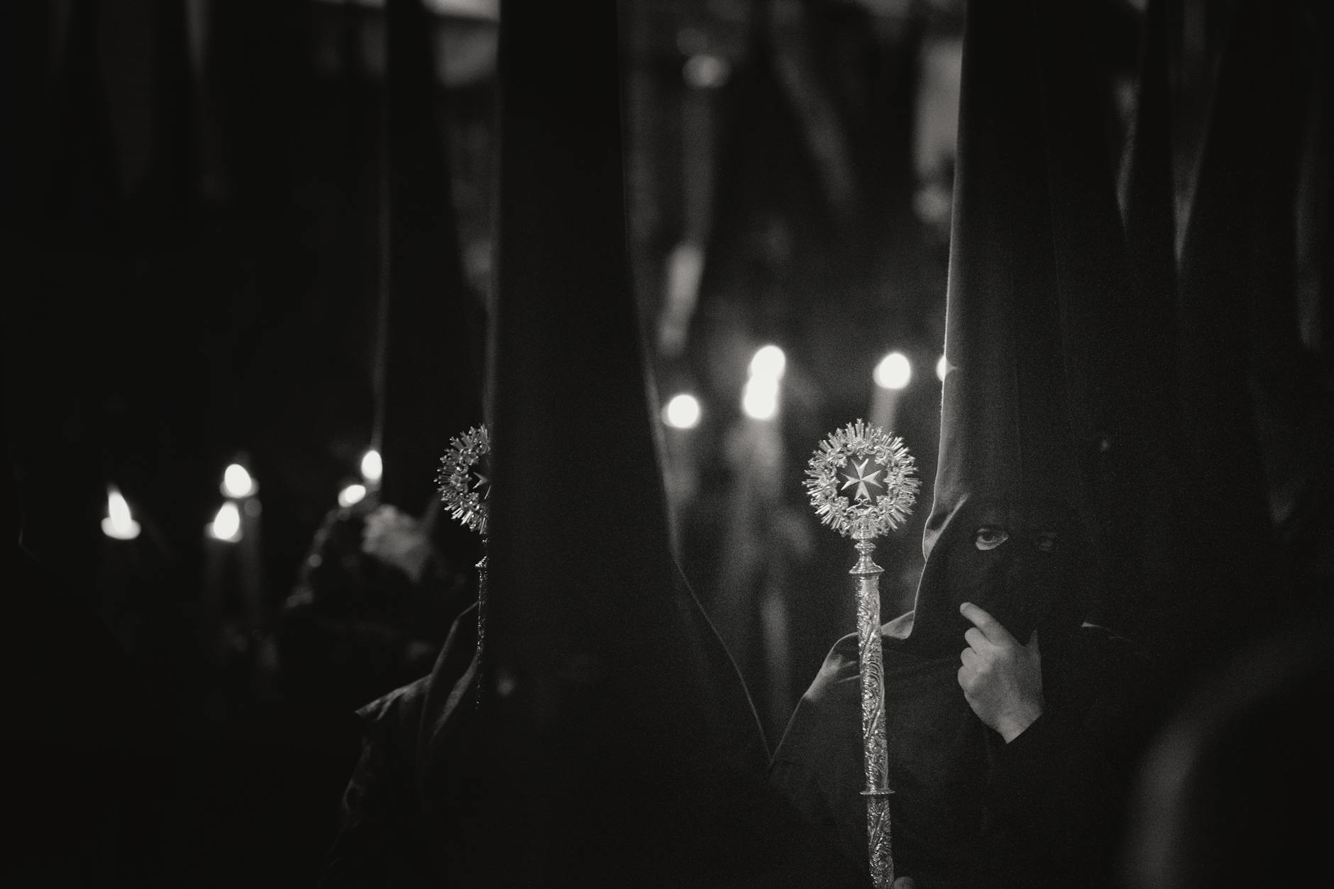 Nocna procesja religijna, uczestnicy w kapturach niosą zapalone świece