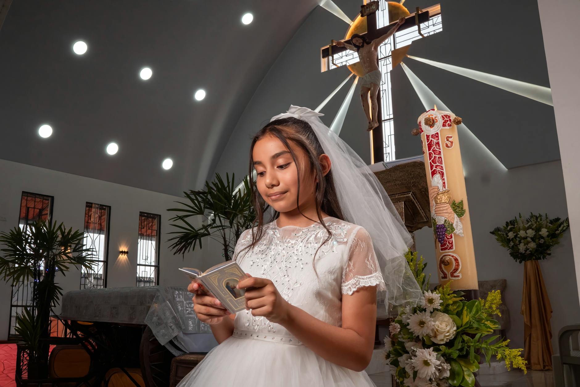 Dziewczynka w białej sukience czyta podczas uroczystości pierwszej Komunii