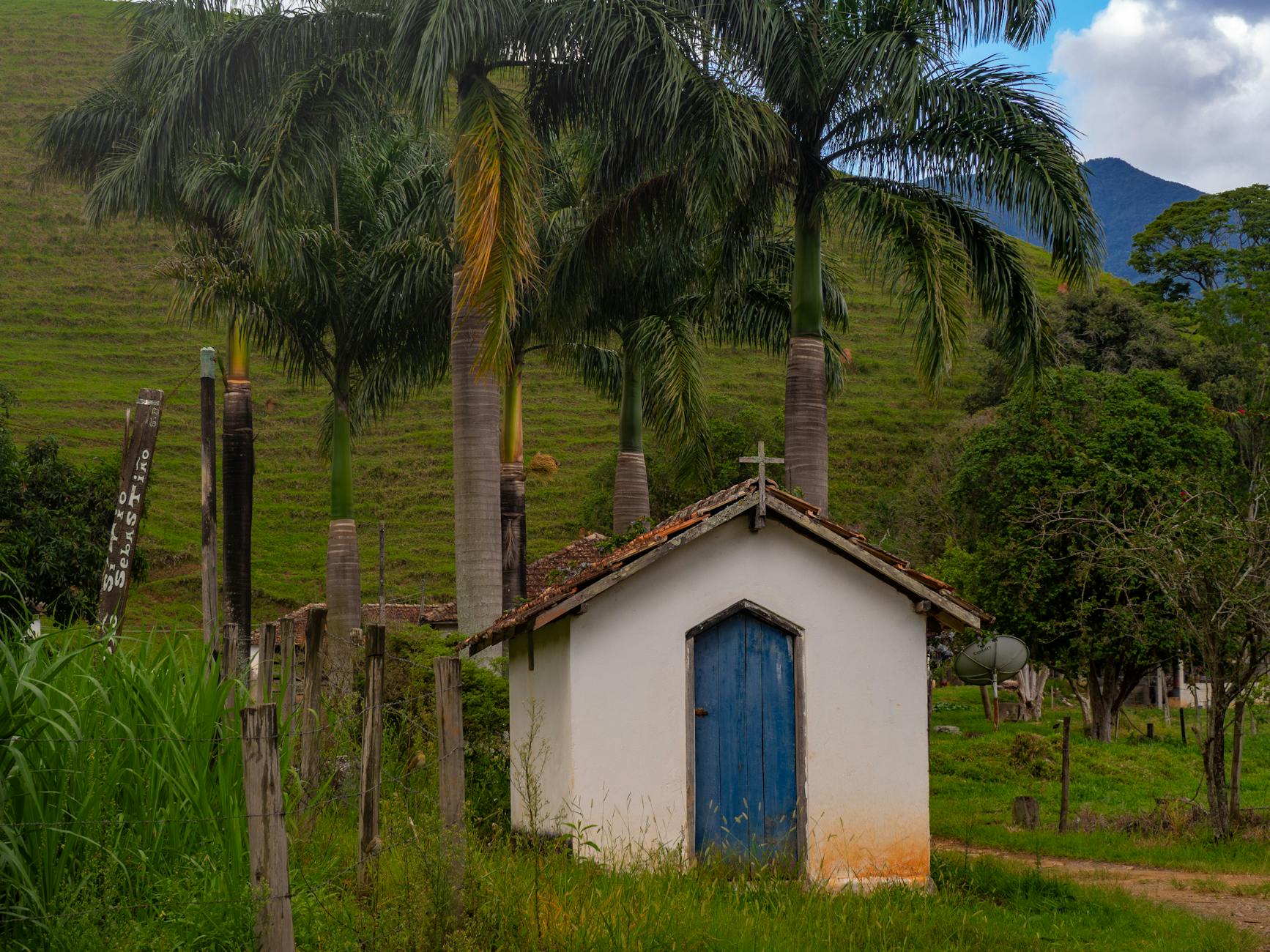 Mała wiejska kapliczka wśród zieleni i palm pod błękitnym niebem
