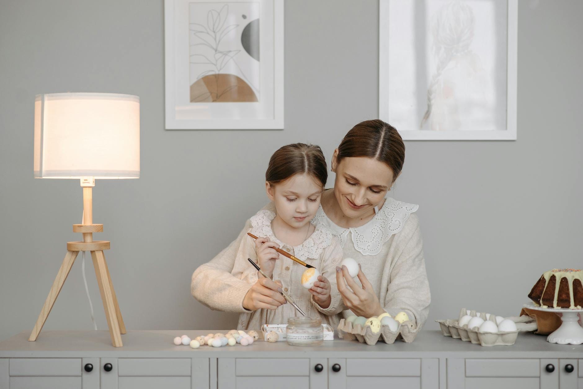 Mama i córka malują pisanki przy stole w domu