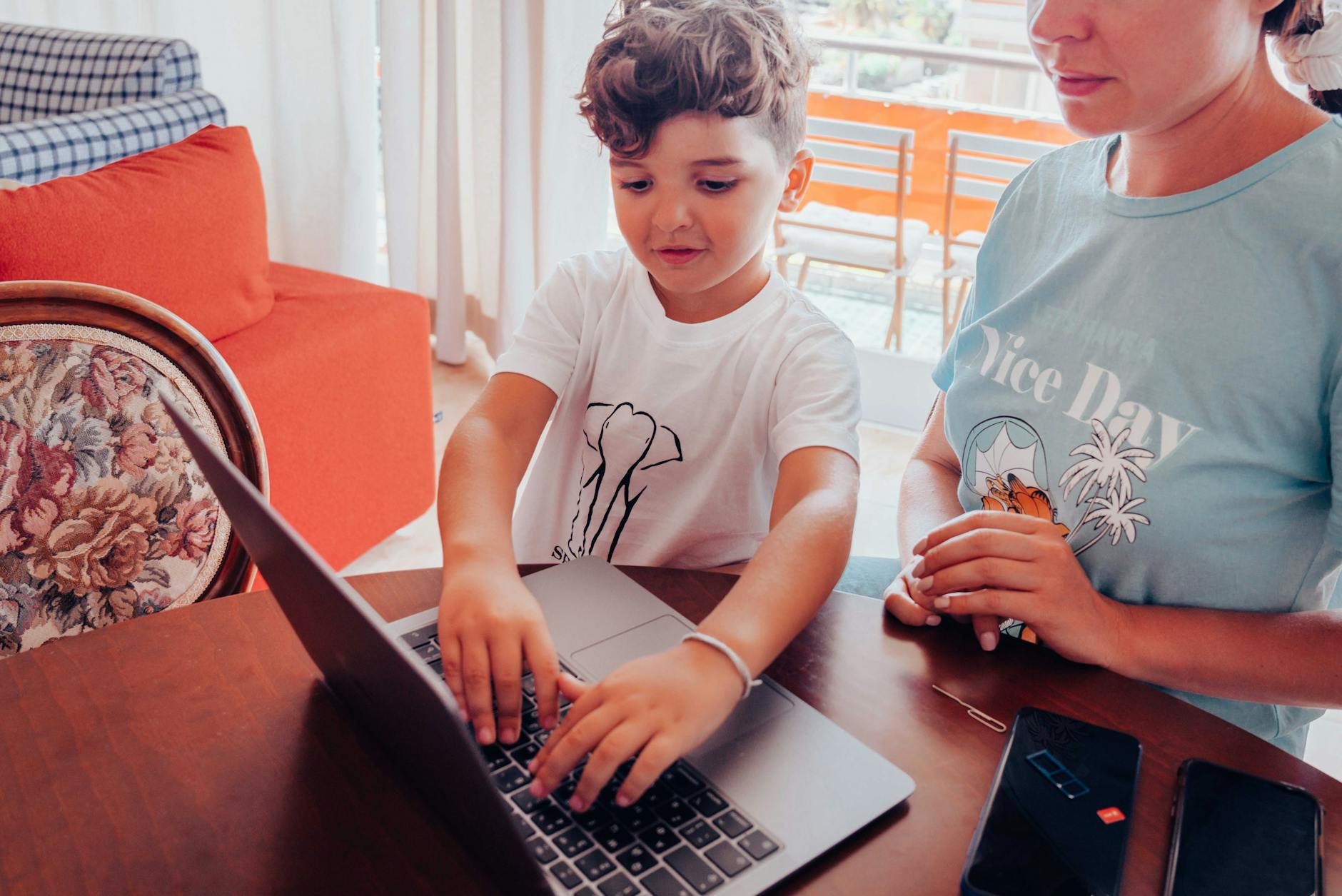 Mama z dzieckiem przy stole korzystają razem z laptopa w domu