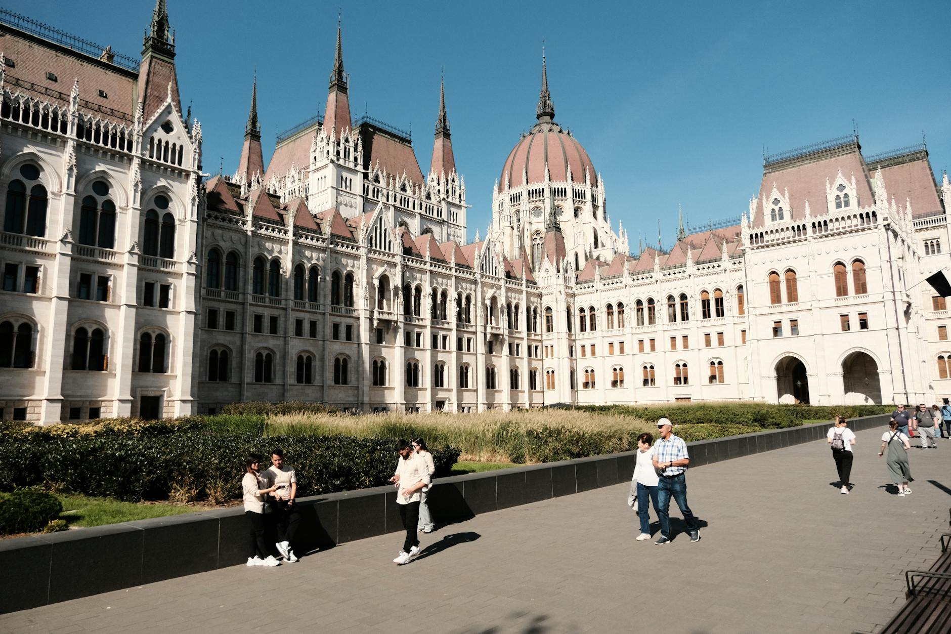 Parlament w Budapeszcie w słoneczny dzień, ludzie spacerują nad Dunajem