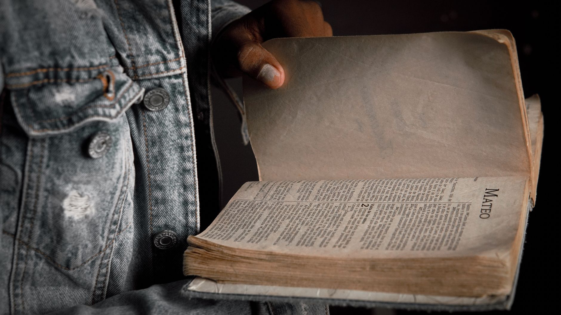 Osoba w dżinsowej kurtce trzyma otwartą Biblię na Ewangelii Mateusza