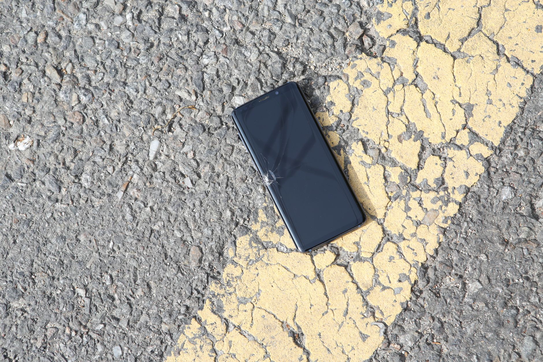 Pęknięty smartfon leżący na nasłonecznionej asfaltowej drodze